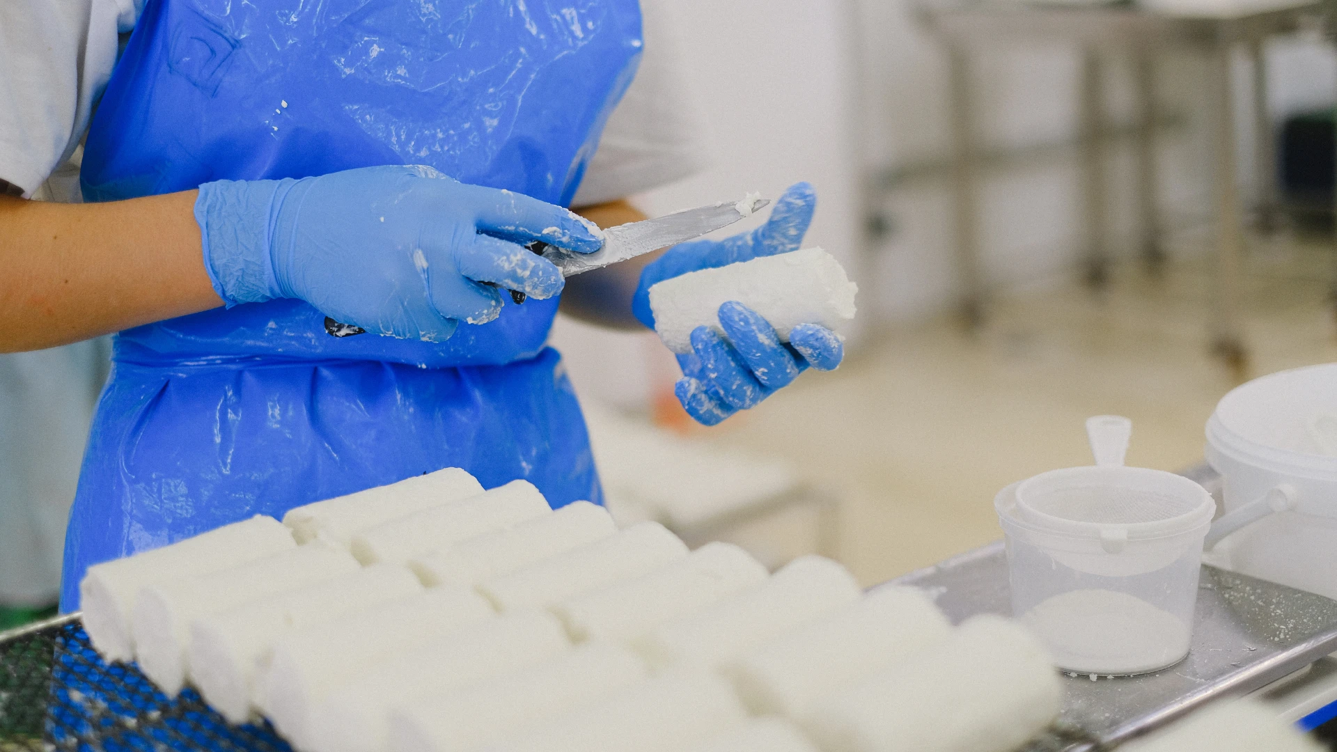 Medewerker met blauwe handschoenen snijdt een wit product in blokken